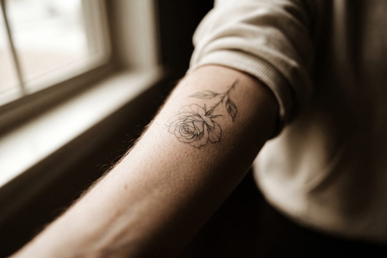 Fine-line single-needle rose tattoo on a forearm in soft natural light