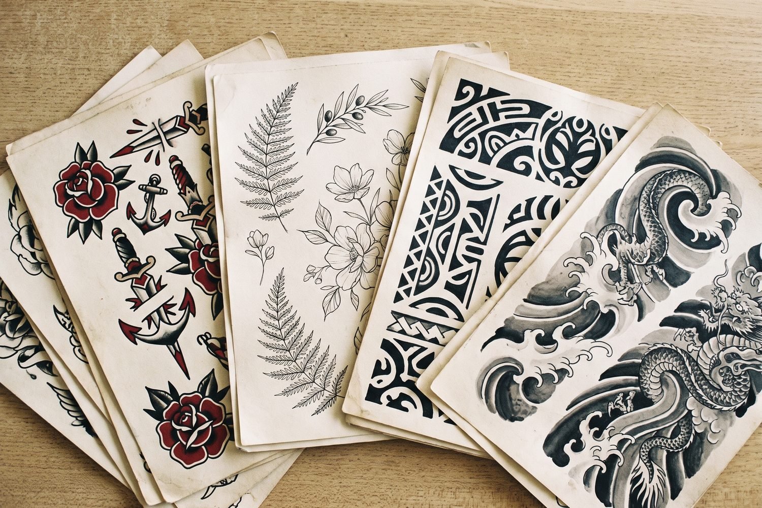 Tattoo flash sheets in traditional, fine-line, tribal and Japanese styles fanned out together